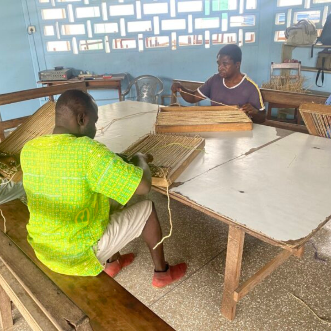 Two young men learning how to weave in a workshop.